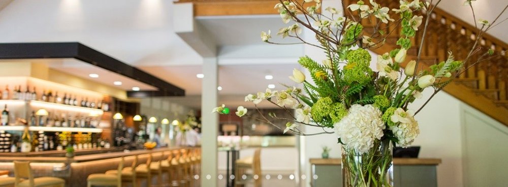 The lobby of a gorgeous hotel with a vase of flowers and a bar in the background.