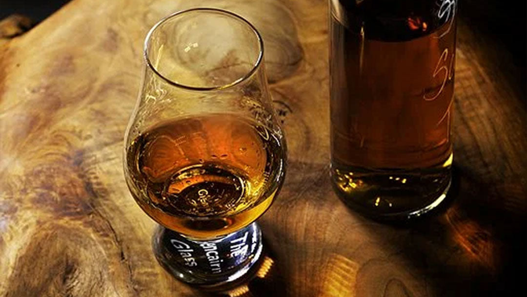 A glass of amber bourbon sitting on a wooden table.