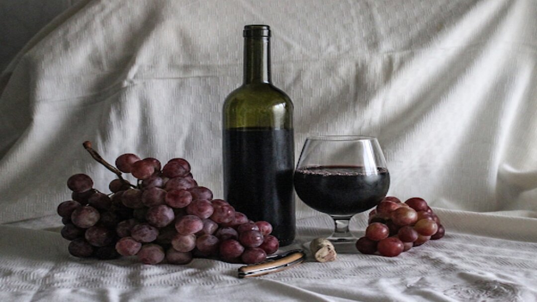 red grapes, a glass of wine, and a wine bottle sitting on a white sheet