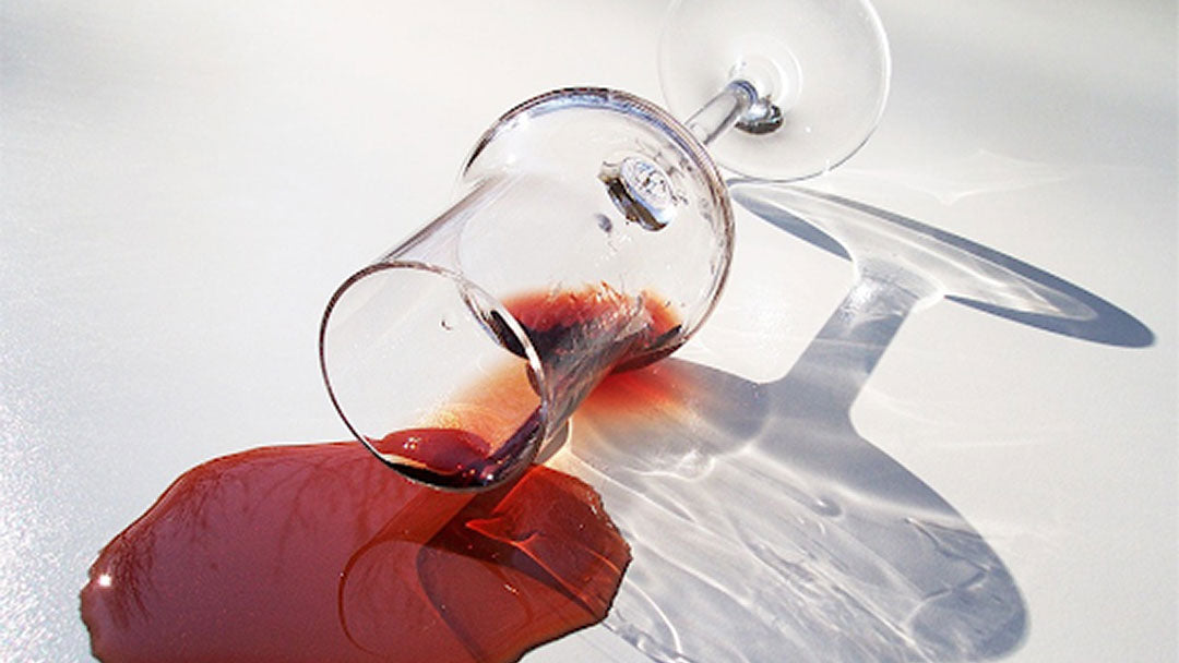 A stemmed wine glass spilling red wine onto a white floor