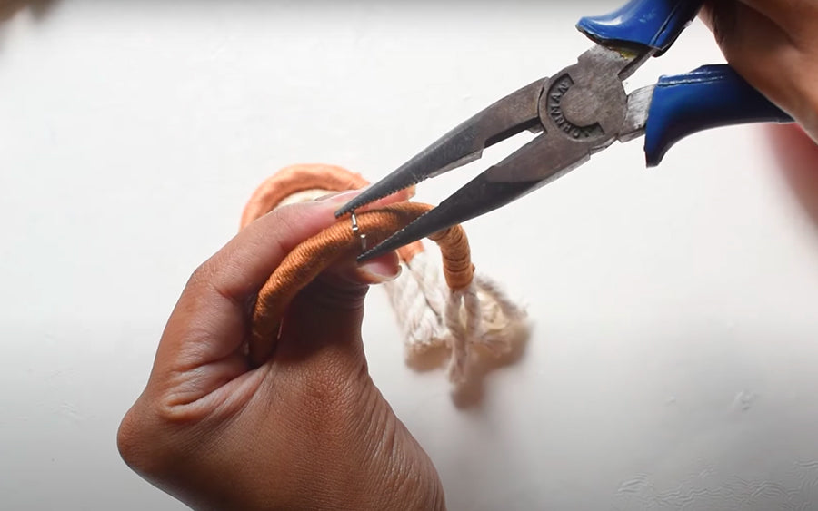 femme qui fixe un pendentif type anneau métallique de porte clé sur un brin de corde colorée