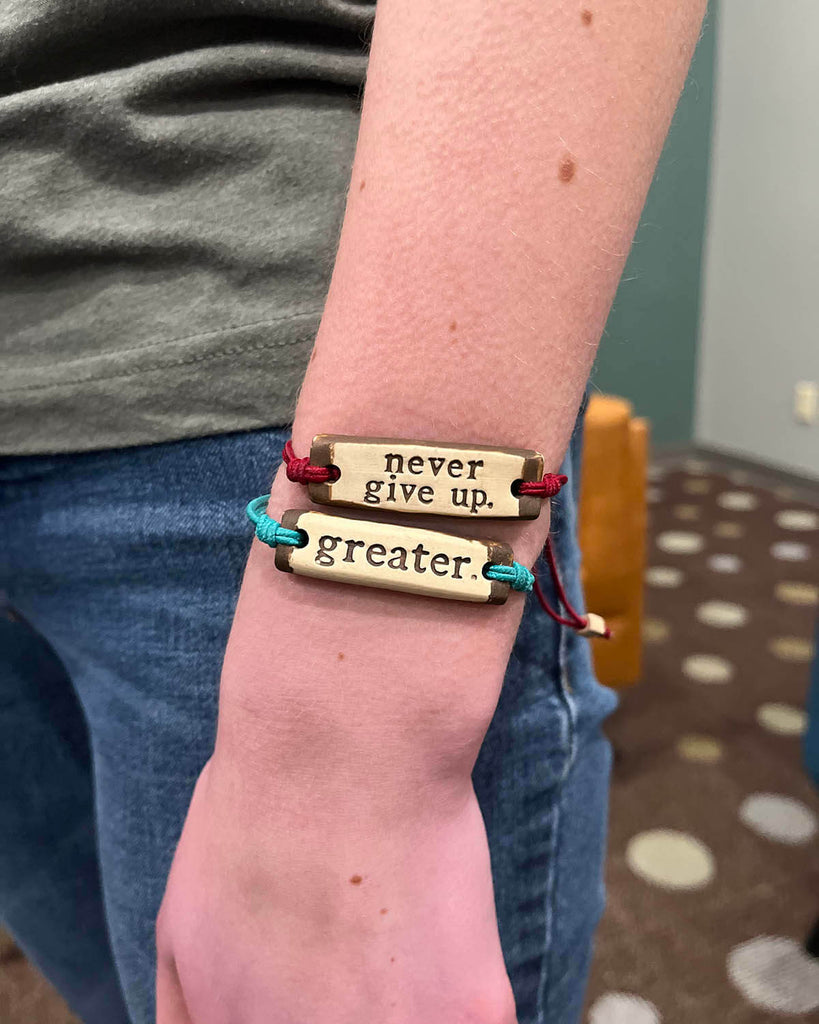 "never give up." and "greater." bracelets