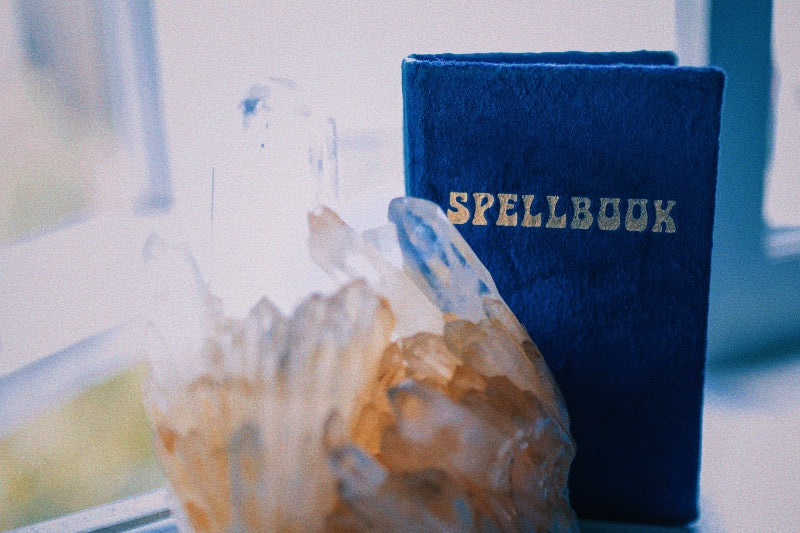 An image of a blue velvet spell book sitting on a windowsill next to a large Citrine crystal.
