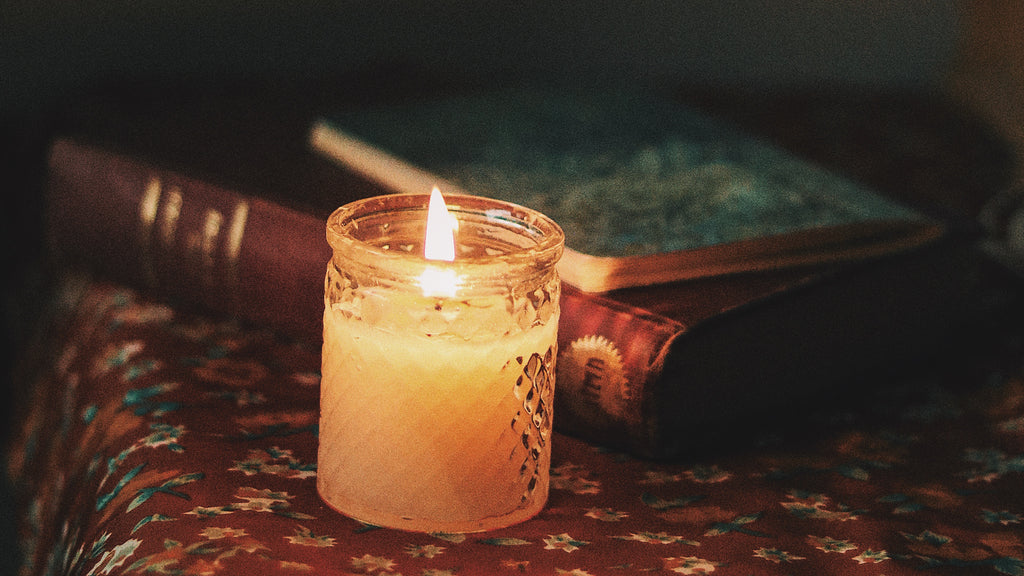 An image of a glass candle with a flame sits on a nightstand with books.
