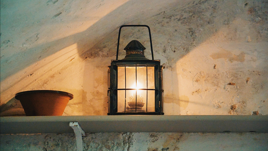 A lone lantern sits atop a shelf casting light on the surrounding white walls worn with age and tarnish.