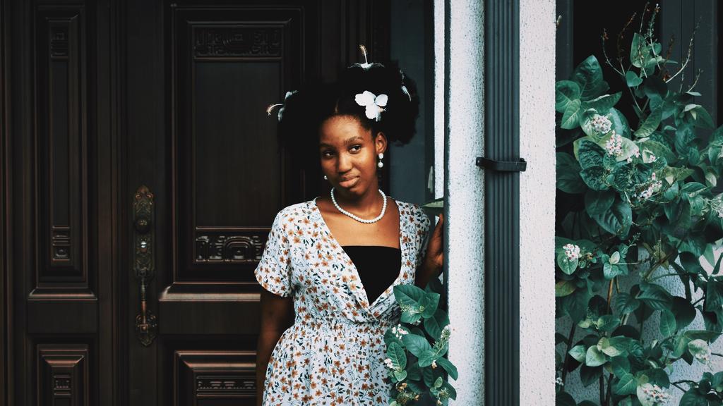 An image of an African-American woman in a white and black dress standing on ornate front porch with ivy vines representing the sign of Virgo.