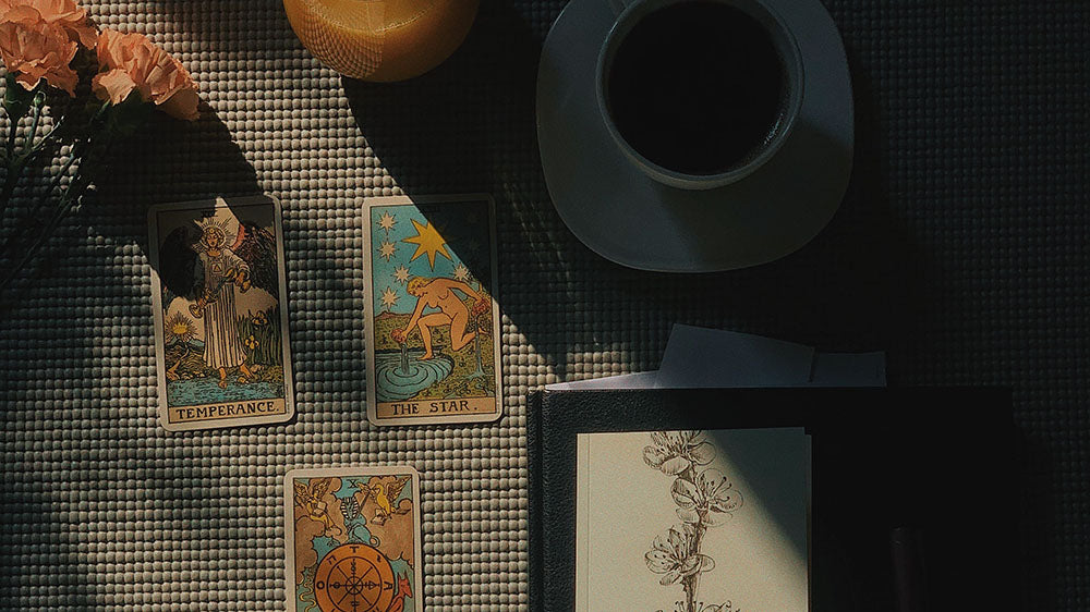 A serene table setting with Tarot cards displaying Temperance and The Star, accompanied by a cup of coffee and flowers in soft light, suggesting introspection and guidance.