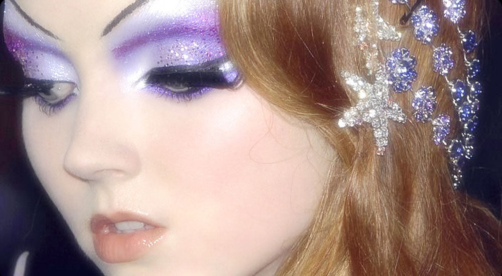 A person's face with dramatic purple eye makeup and shiny crystal hair accessories, radiating a sense of celestial elegance meant to be the Goddess Asteria