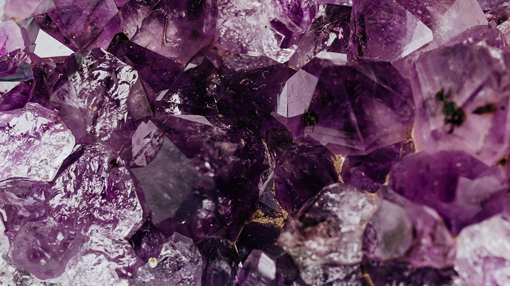 A close-up of a sparkling amethyst crystal, showcasing its vibrant purple color and natural geometric facets.