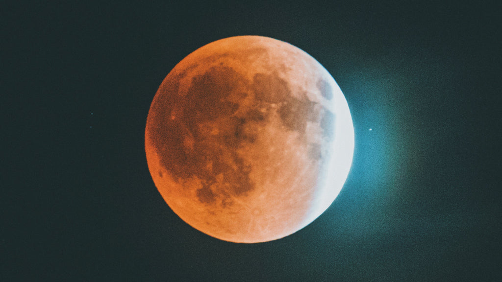 "A striking image of the Full Blood Moon, glowing in a deep reddish hue against a dark sky, with a hint of starry specks visible in the surrounding cosmos, signifying its presence in the zodiac sign of Taurus."