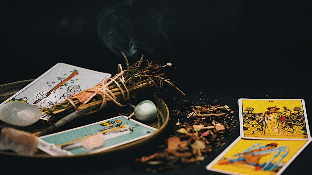 A tarot spread with smudging herbs and crystals on a dark surface, indicating guidance and reflection under the Cold Moon.