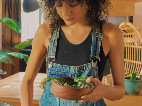 Curly haired girl making new moon rosemary hair growth oil in a boho style kitchen.