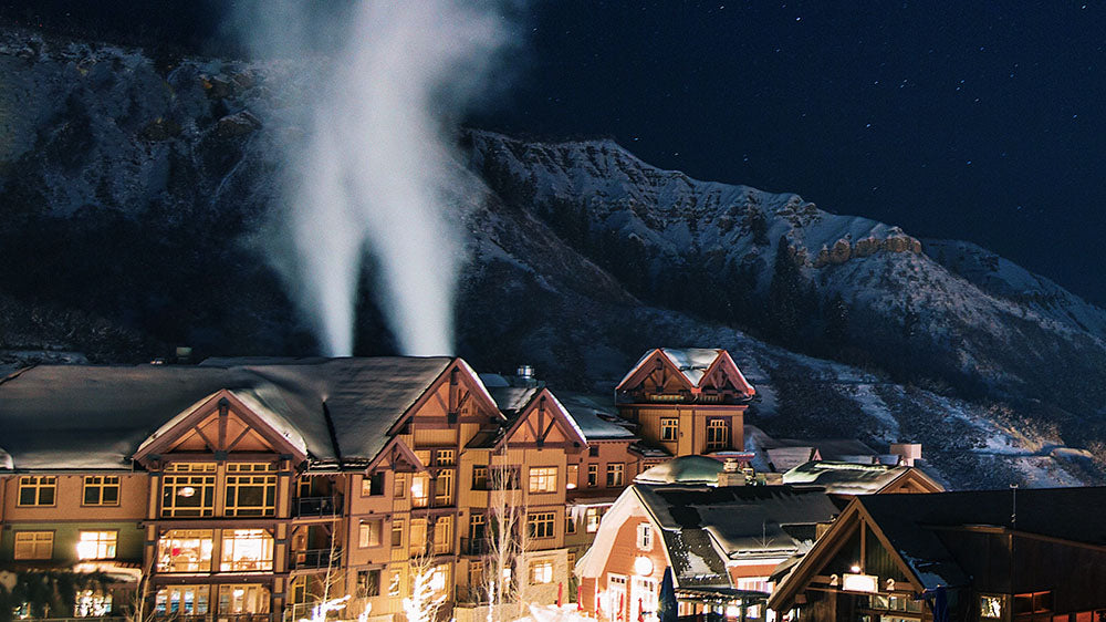 A nighttime scene of a snow-covered mountain village lit by warm lights, the steam rising in the cold air, which can be associated with the communal and structured spirit of Capricorn on the New Wolf Moon.