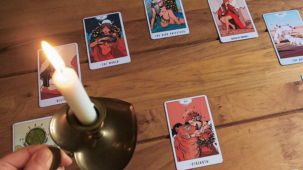 A lit candle in a brass candlestick holder illuminates a selection of tarot cards spread on a wooden surface, evoking a mystical atmosphere for a New Year's tarot reading.