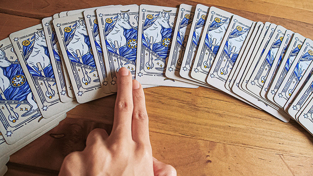 A hand hovers over an array of tarot cards face down on a wooden table, poised to select one, symbolizing the anticipation of unveiling the year's fortunes.
