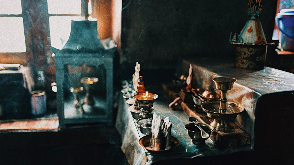 A mystical altar bathed in the warm, diffused light of a secluded room, capturing the essence of the New Oak December Moon in Sagittarius. Ritualistic objects, including candles emitting wisps of smoke, brass bowls, a ceremonial cup, and an ornate bell, are thoughtfully arranged on a cloth-covered table. The scene evokes the expansive and spiritual energy of Sagittarius, inviting reflection and introspection during this lunar phase.