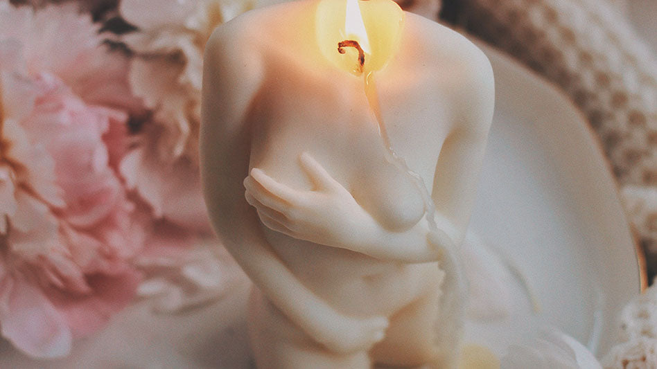 Burning sculpted candle depicting a feminine figure with soft pink petals in the background, symbolizing the rituals for embracing Aphrodite's love and beauty.