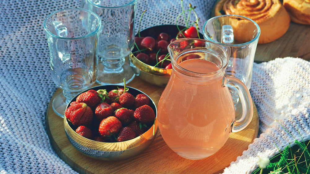 Strawberry Moon Picnic: A picnic setup with fresh strawberries, cherries, glasses, and a pitcher of strawberry-infused drink, capturing the essence of celebration and nourishment under the Strawberry Moon.