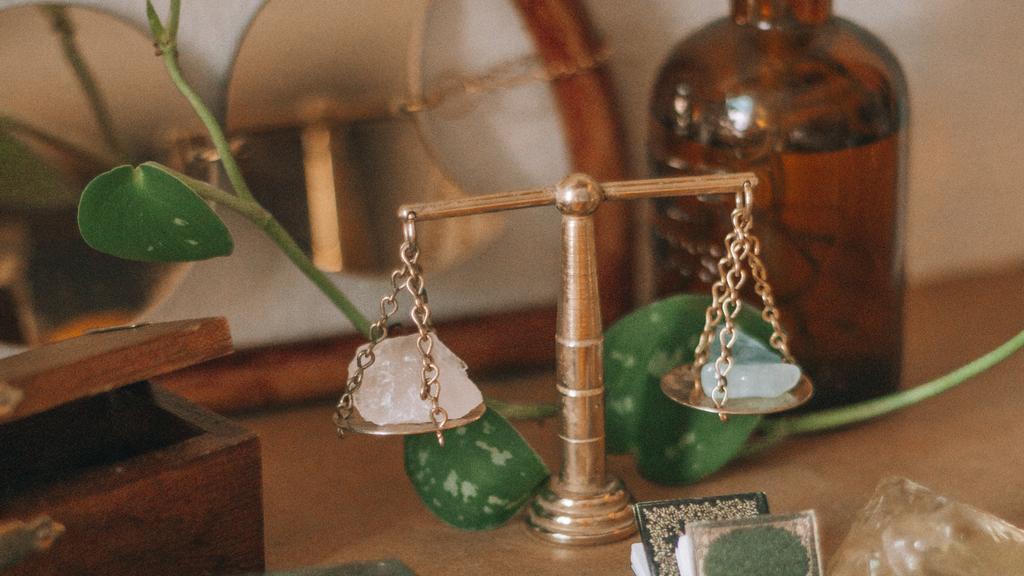 Golden scales delicately balance crystals on a witch's altar covered in amber-colored bottles and plants.