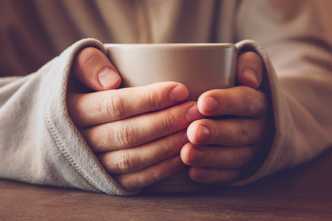 two hands wrapped around a mug of warm tea