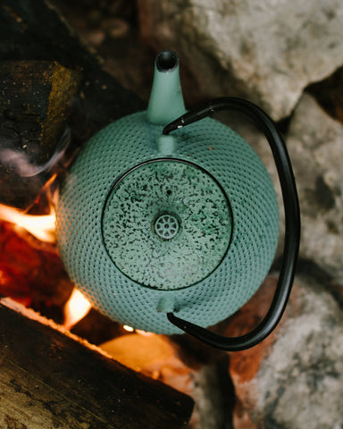 teal teapot being heated over open fire