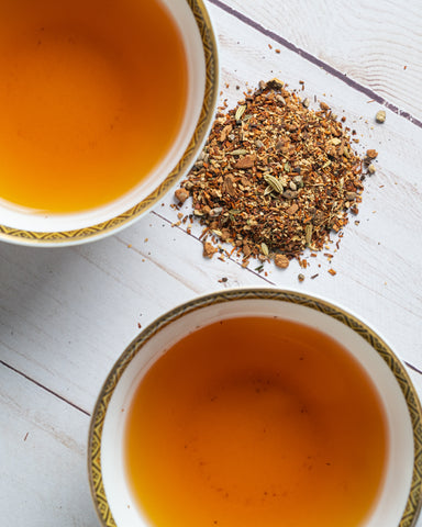 two mugs of brewed tea, loose leaf tea between them