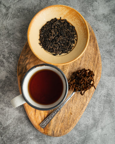 a mug of steeped tea beside a bowl and spoonful of tea leaves