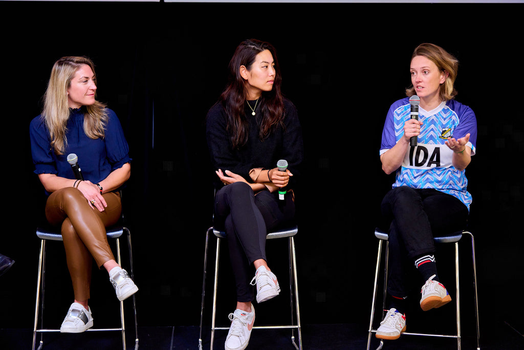 IDA co-founder Laura Youngson sits in a stool on stage speaking on a microphone alongside 3 other female founders at an event with the Trailblazer Venture Studio.