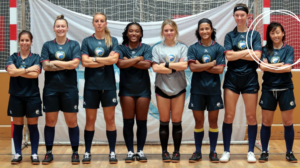 8 female futsal players from the US Futsal Women's National Team stand in a line in front of a futsal goal with crossed arms and wearing the Ida Spirit at the 2022 IFA World Championships 