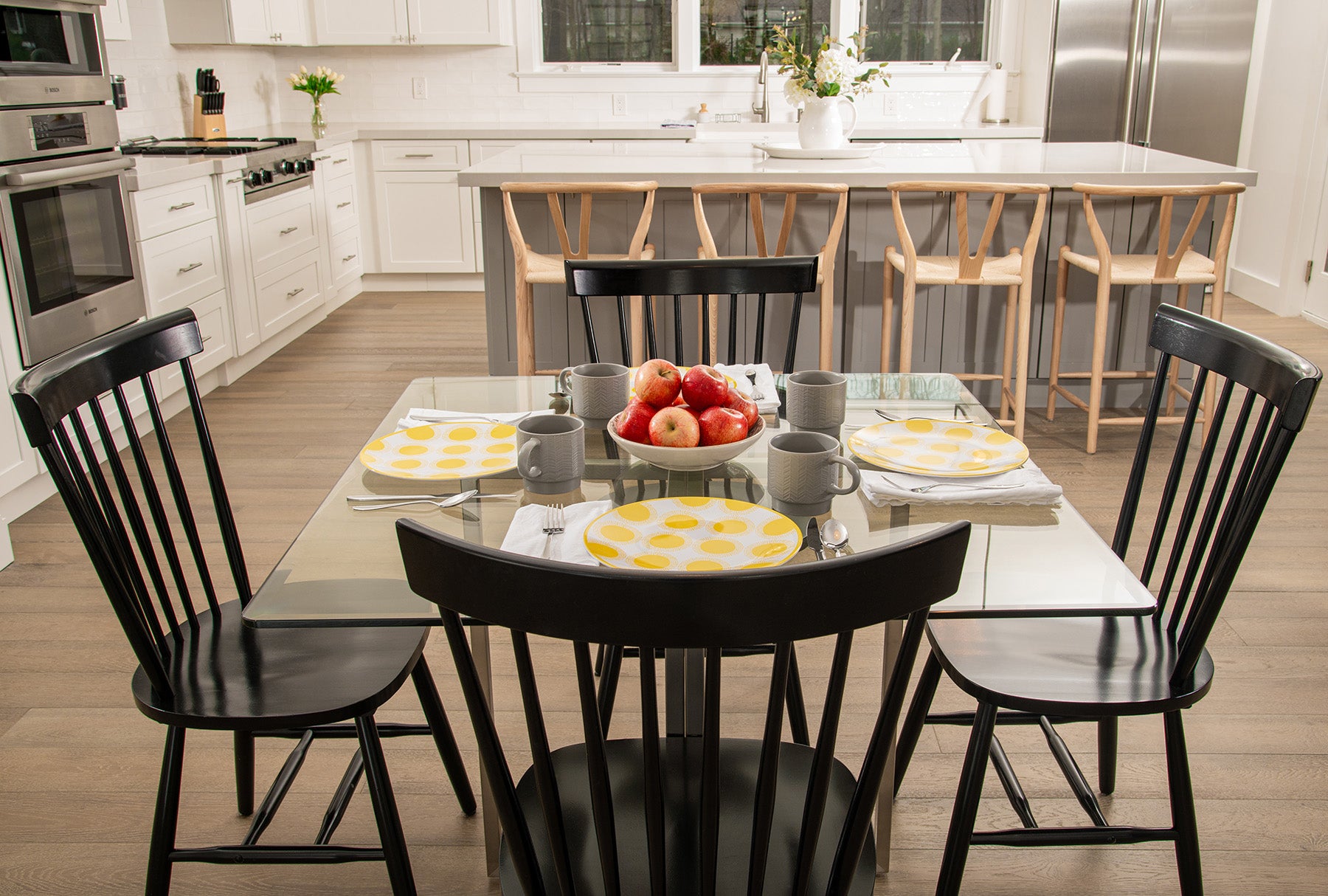 Square glass clear table with yellow polka-dot plates, apples in the middle, and four black wood chairs
