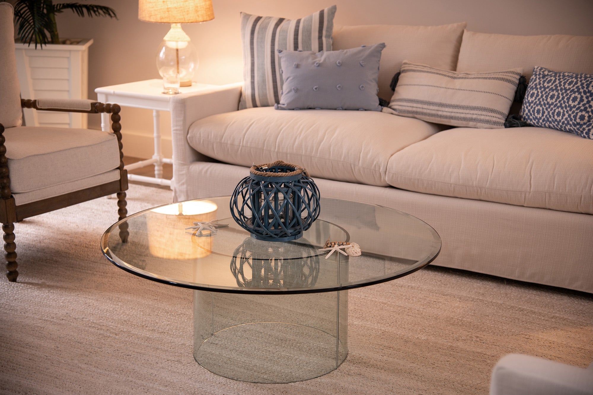 Round clear glass table on cylindrical glass base with bevel edges next to white couch