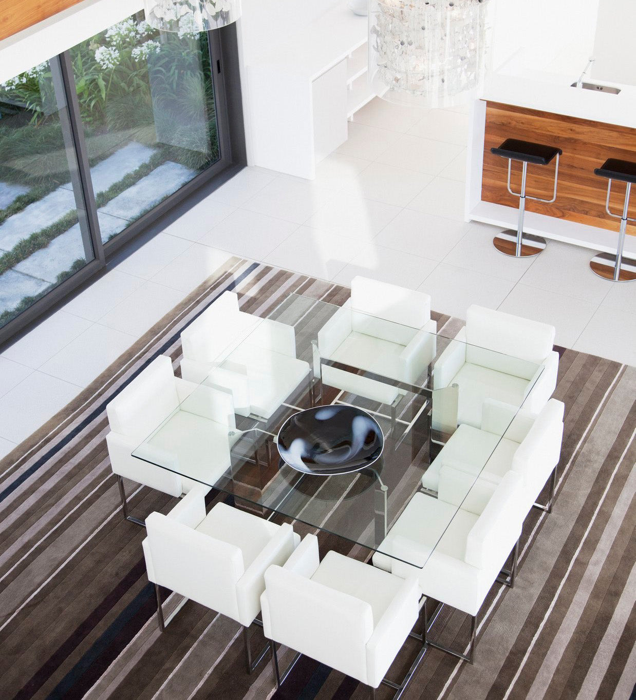 Large square clear glass table in the distance with eight white chairs and large brown flat bowl in the center