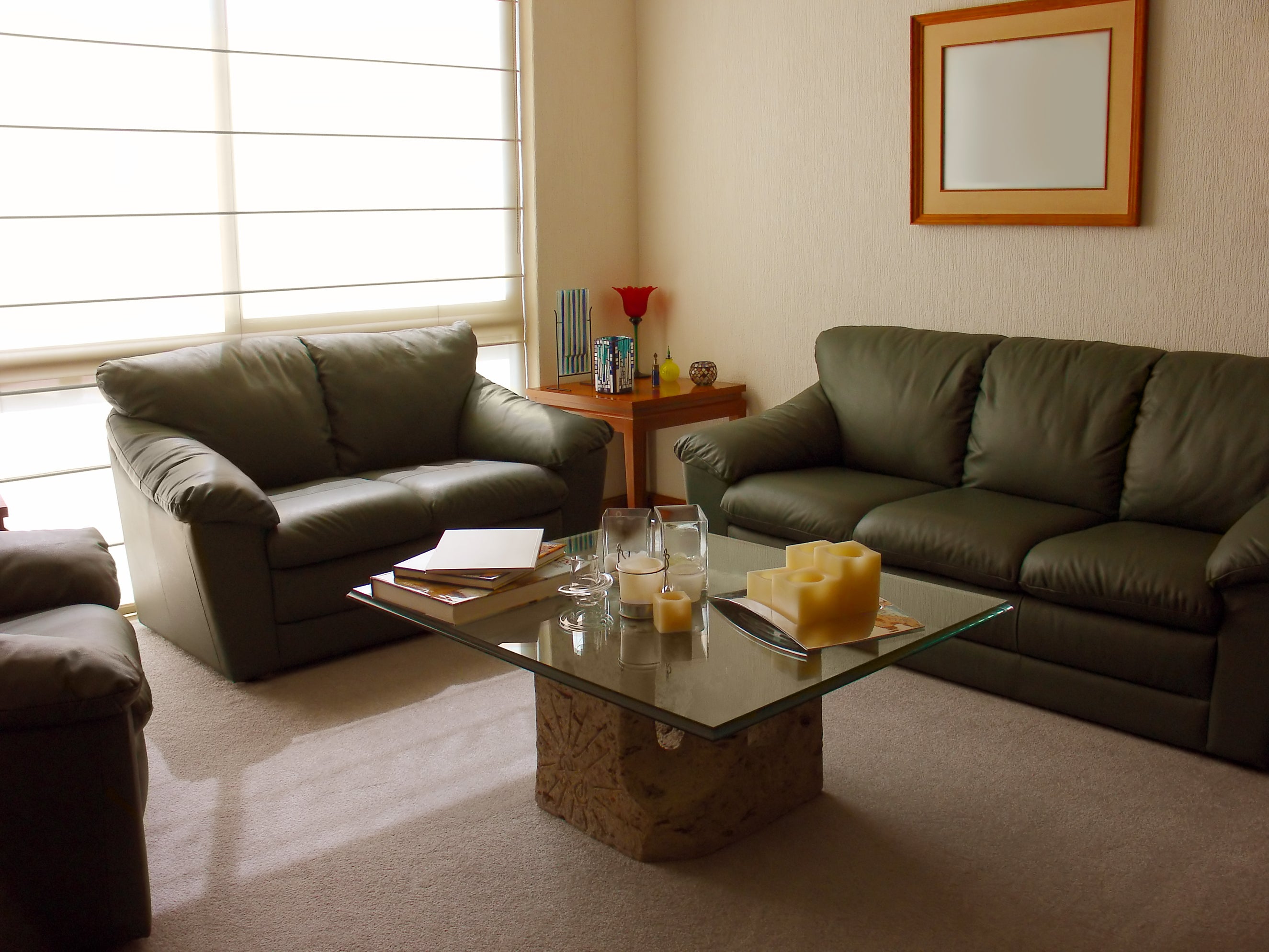 Square clear glass table placed between three pieces of dark leather couches with a tan stone base