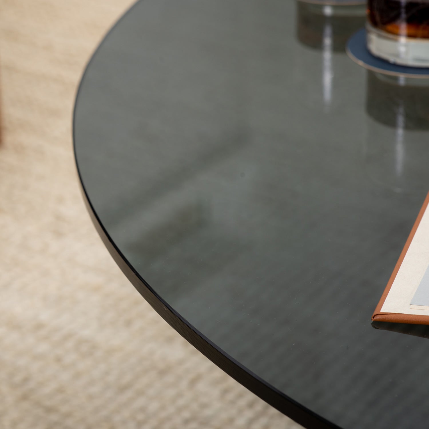 Round grey glass table top showing with bronze metal base with glasses and a book on top