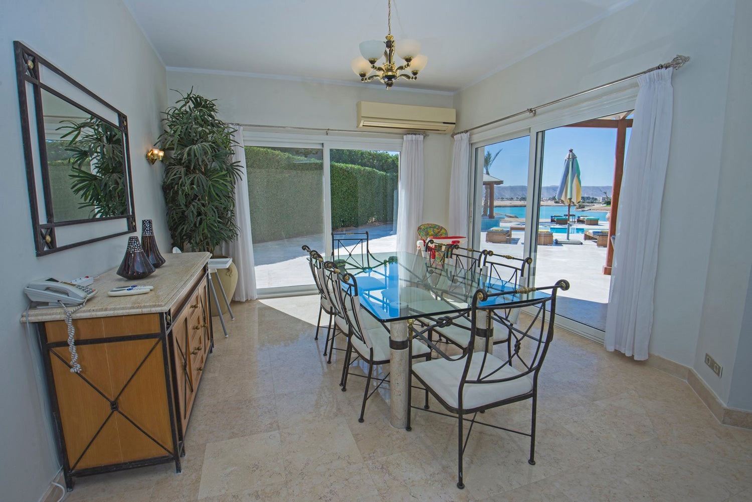 Rectangle clear glass table with eight thin metal chairs in a corner room with two large glass sliding doors