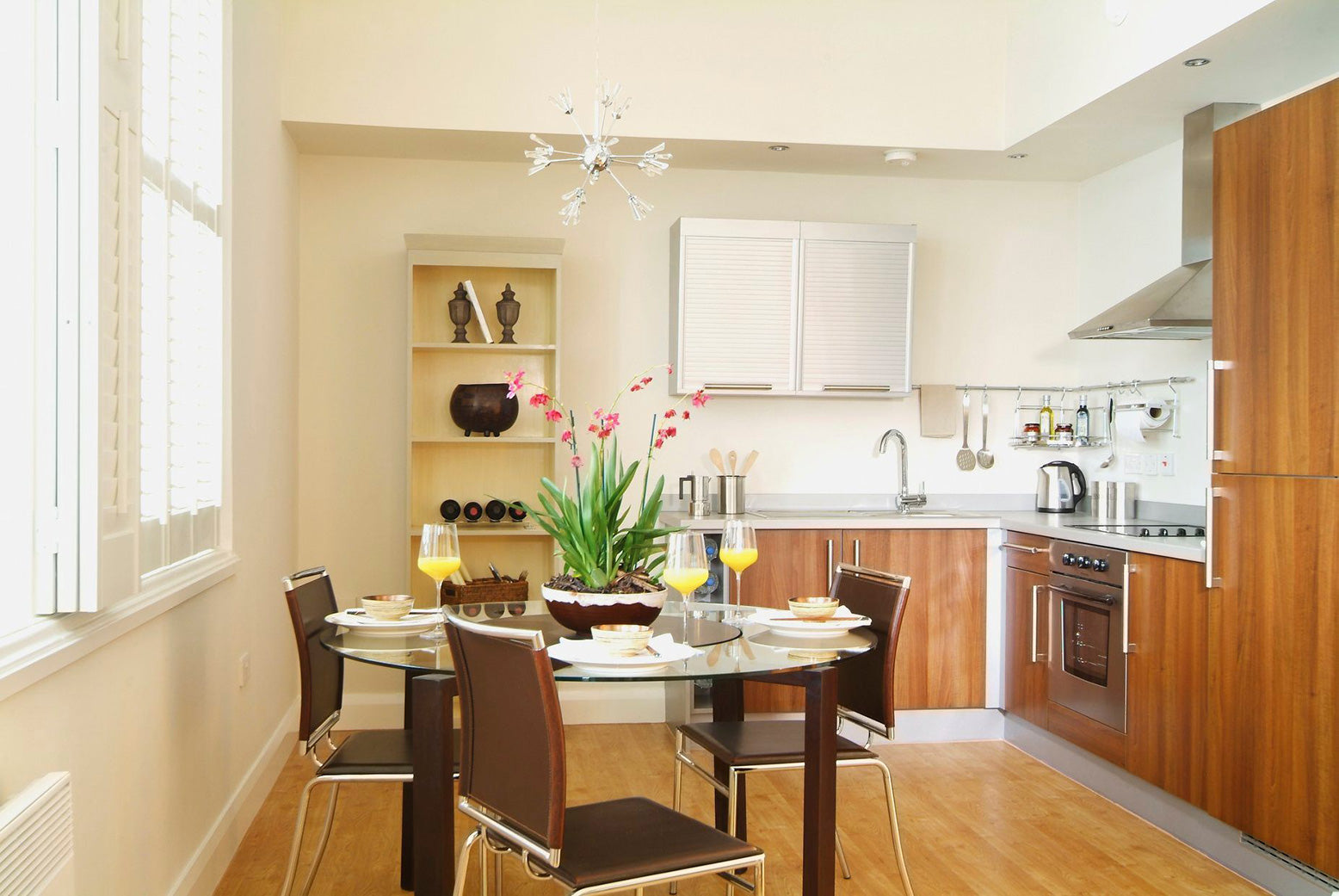 Round clear glass table with clear glass base with steel chairs and brown cushions in kitchen