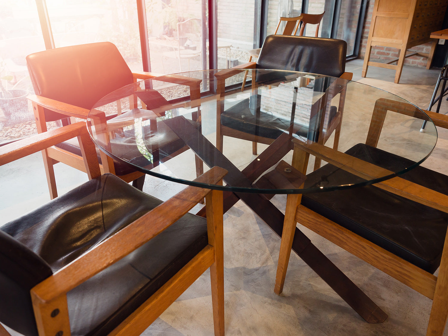 Round clear glass table with four chairs made of wood with black leather cushions surrounding the table