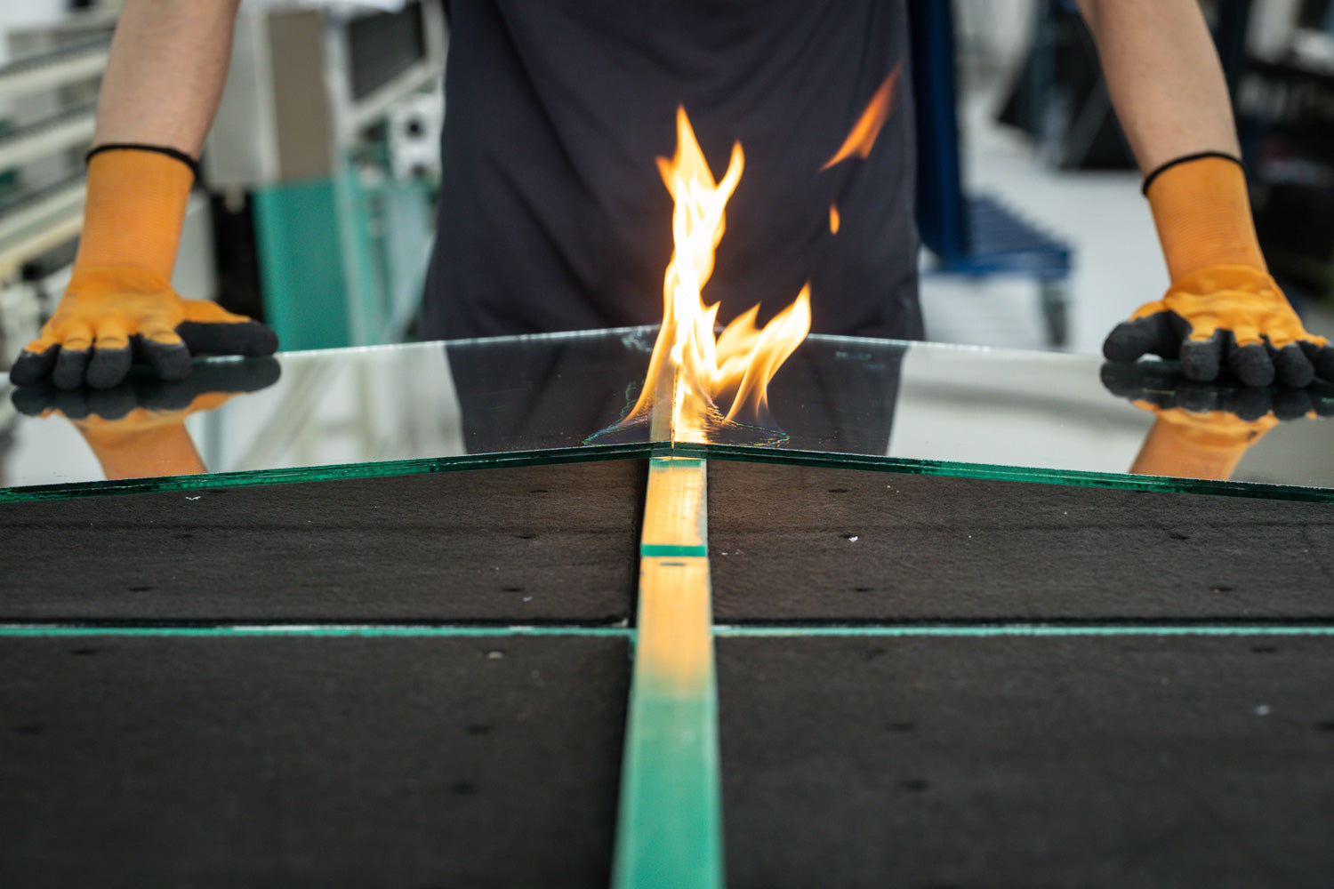 Person with orange gloves holding a piece of clear glass with fire rising from the middle of the glass