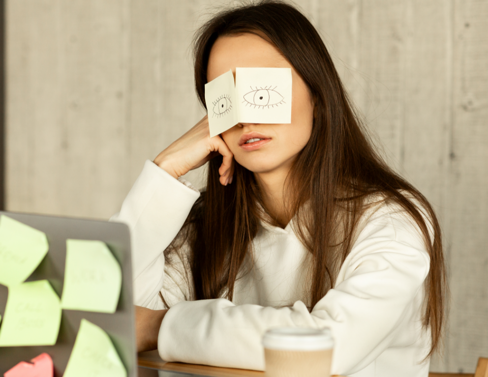 A woman is leaning towards her right hand with a piece of paper covering her eyes.