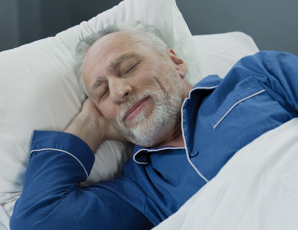 A senior man wearing a blue sleepwear is sleeping soundly.