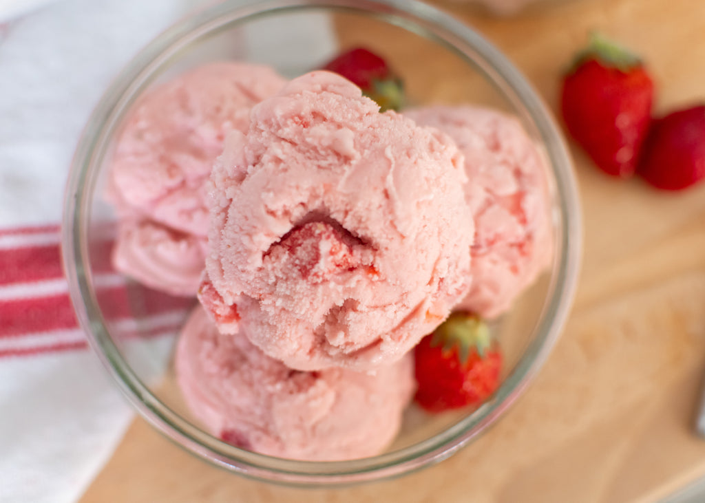 strawberry ice cream made with goat milk scooped into a glass bowl, with strawberries surrounding