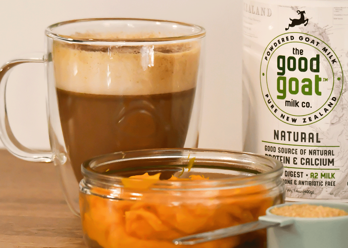 Close up of the pumpkin spiced latte in a clear mug with pumpkin puree in bowl in front and a container of Good Goat Natural Goat milk powder to the left