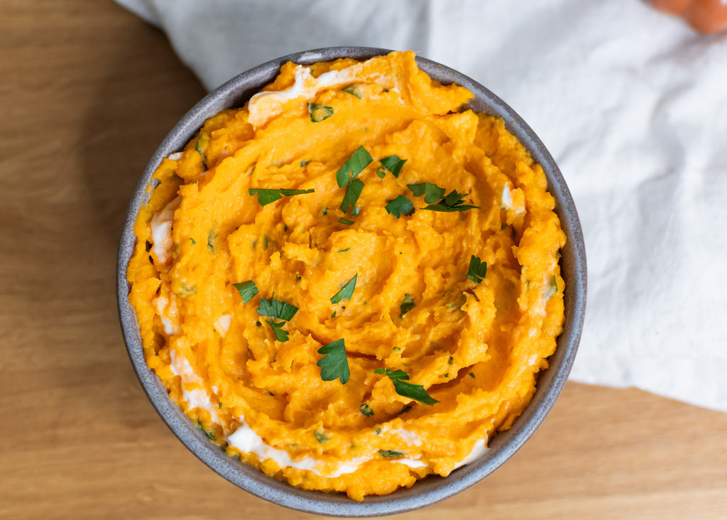 Mashed sweet potatoes in a bowl with fresh parsley on top, made with good goat milk powder, on a white napkin