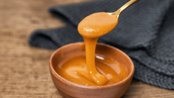 Manuka honey dripping from spoon over wooden bowl