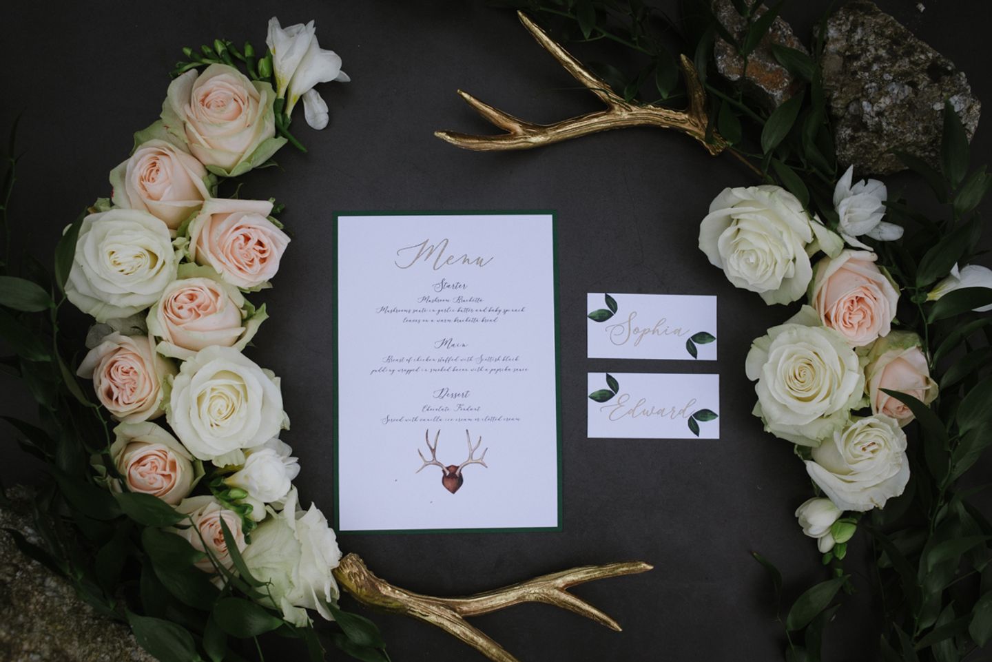 Country House wedding flat lay - gold stag horns and roses adorn modern calligraphy menu and  place cards