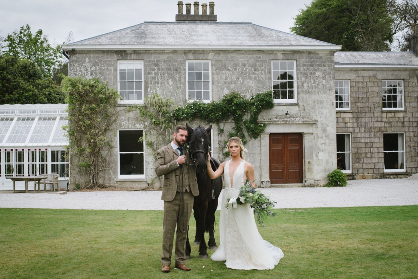 Bride and groom pose with horse in front of Cornish country house