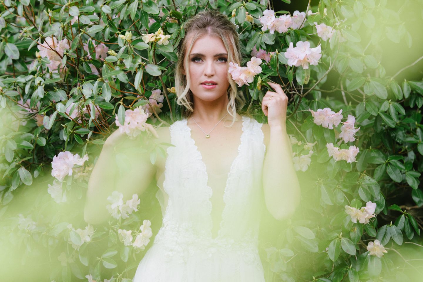 Bride surrounded by pink blossoms in deep plunge lace wedding dress