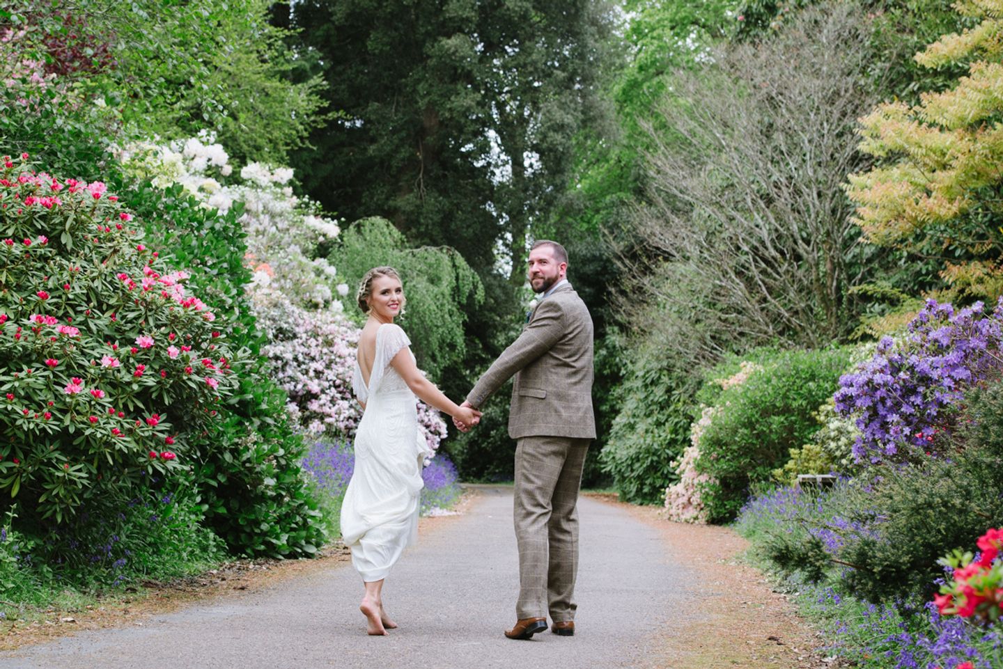 Bride and groom look back towards camera walking through Cornish country house gardens