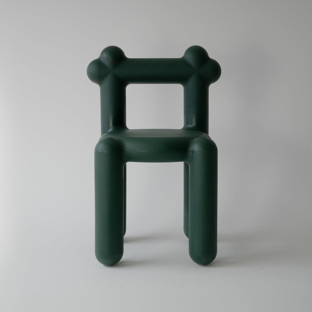 Dark green plastic chair with oversized tubular legs and arms against a white background.
