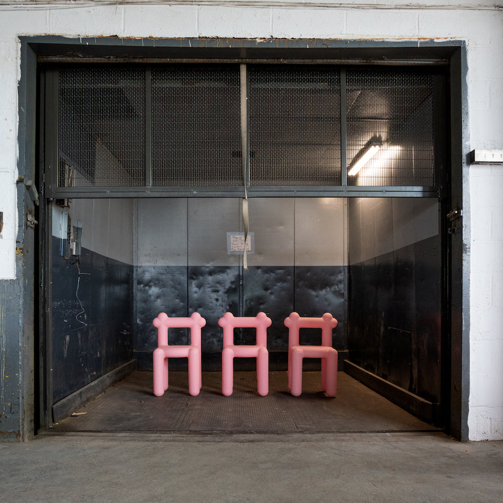 Four pink chairs in front of an industrial freight elevator.